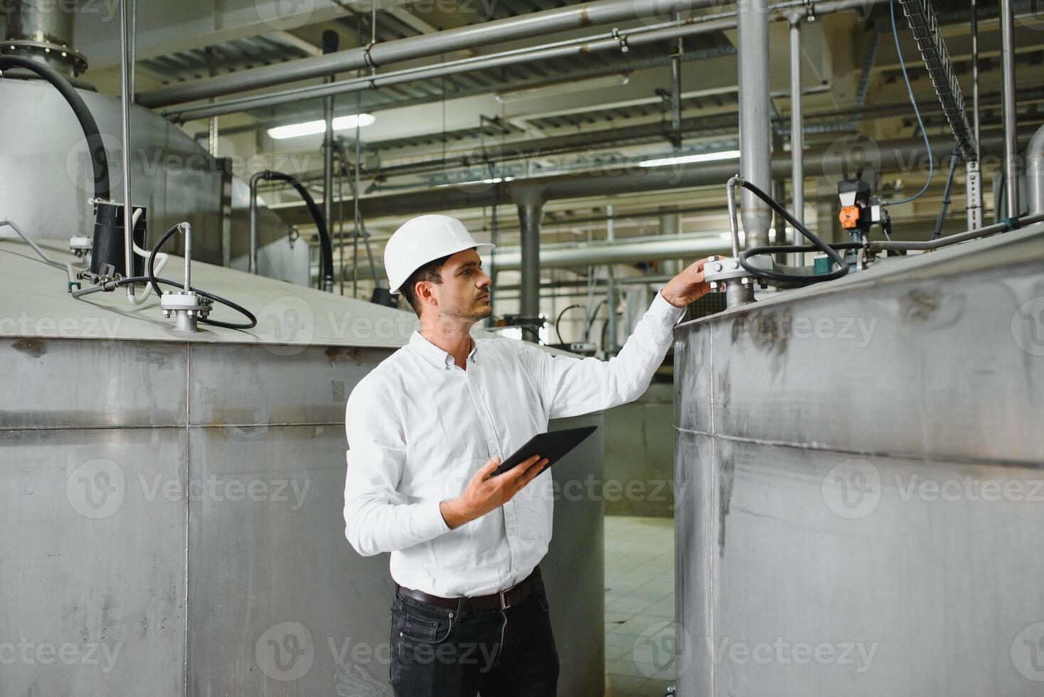 Close up of young Caucasian smiling worker with helmet on head using tablet for work while standing in warehouse. photo
