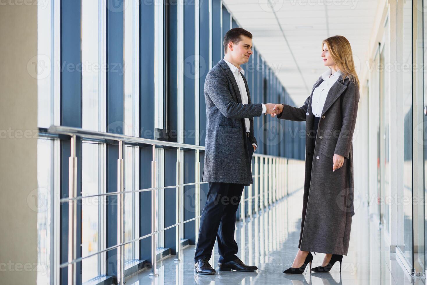 Business men and women shaking hands with a smile on the background of the large panoramic windows in a modern business center. Models dressed in a dark business suits. photo