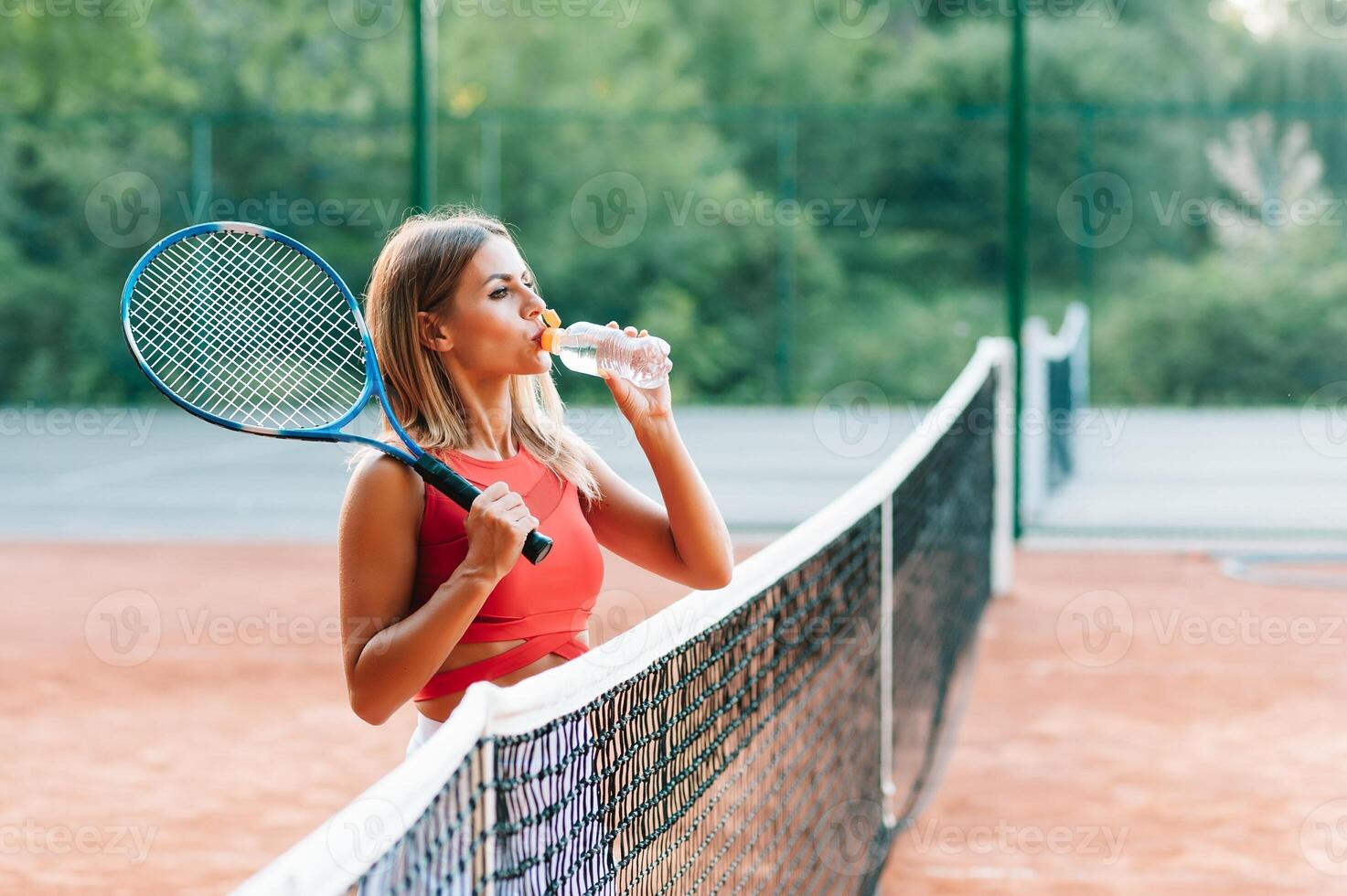 Female tennis player with towel on her shoulders drinking water after match. photo