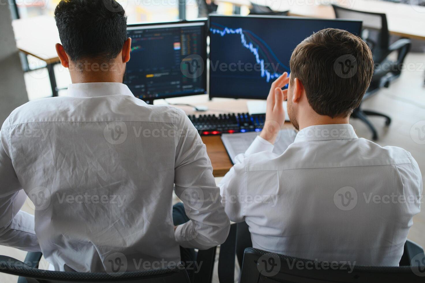 Two successful trader sitting in office and looking at screen, checking cryptocurrency information data on finance market graph, pointing on monitor photo