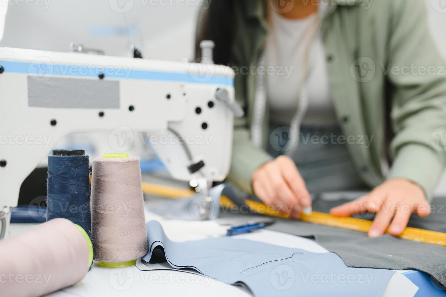 Positive young woman sewing with professional machine at workshop. photo