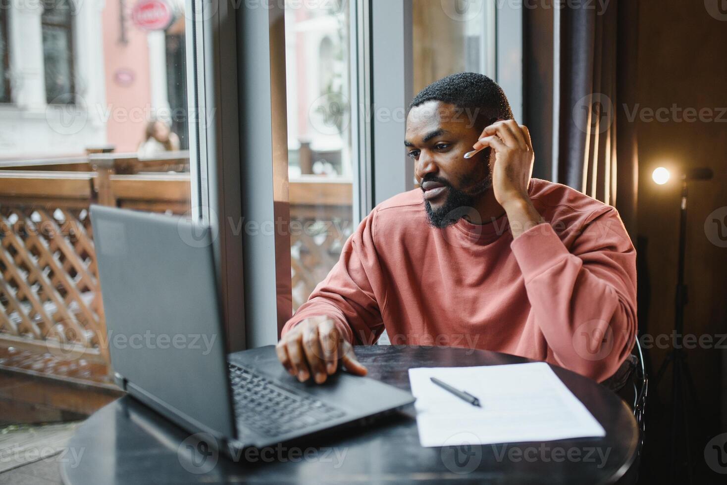 Afro american talks video chat on computer sits in cafe with cup of coffee. Black man calls on laptop on video link and speaks. He wears in shirt and suit jacket. Video link online connection photo