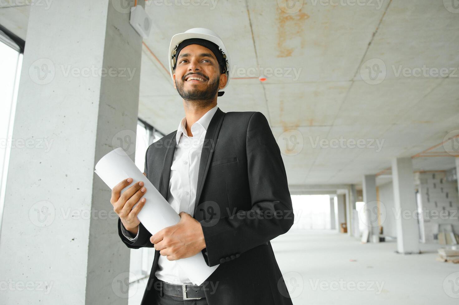Indian construction site manager standing wearing helmet, thinking at construction site. Portrait of mixed race manual worker or architect. photo