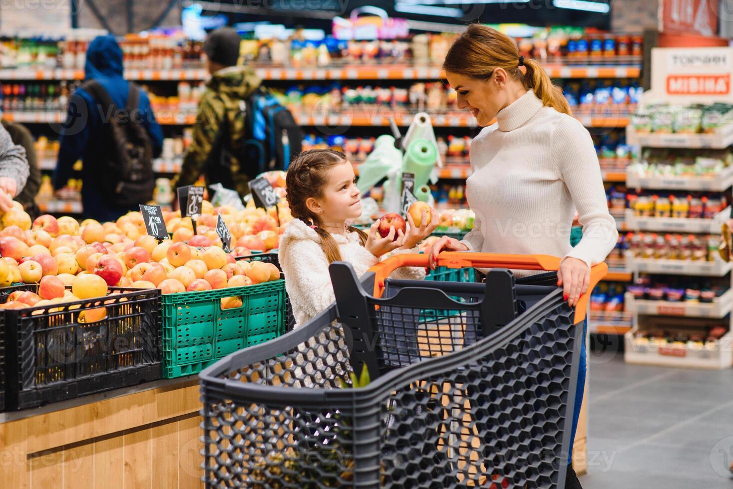 hermosa madre participación tienda de comestibles cesta con su niño caminando en supermercado. compras para saludable. foto