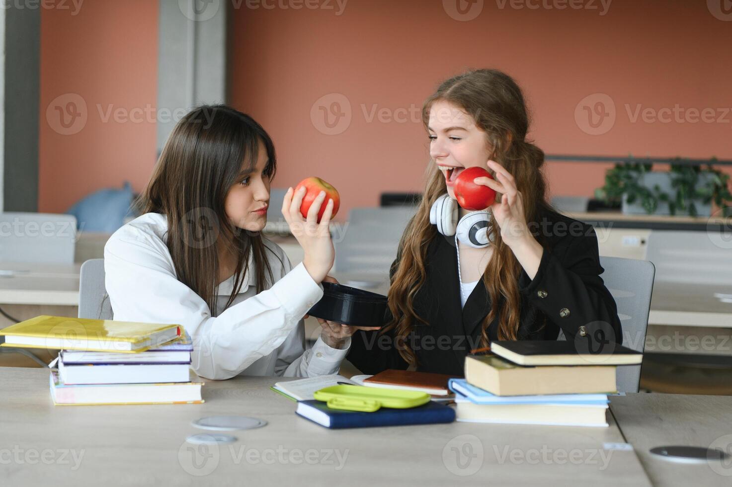 Two happy smiling female students are sitting and eating apples, studying and preparing for exams. photo