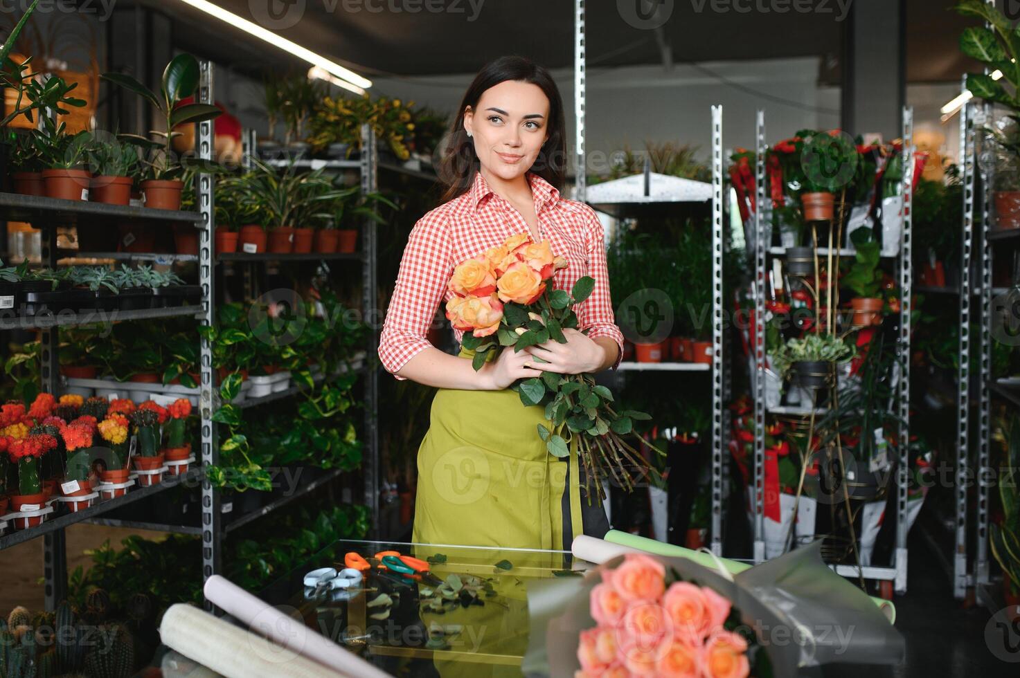 Cute girl florist collects a bouquet of roses in a flower shop. A beautiful florist creates a composition of flowers. Girl cuts flowers and removes stale leaves photo