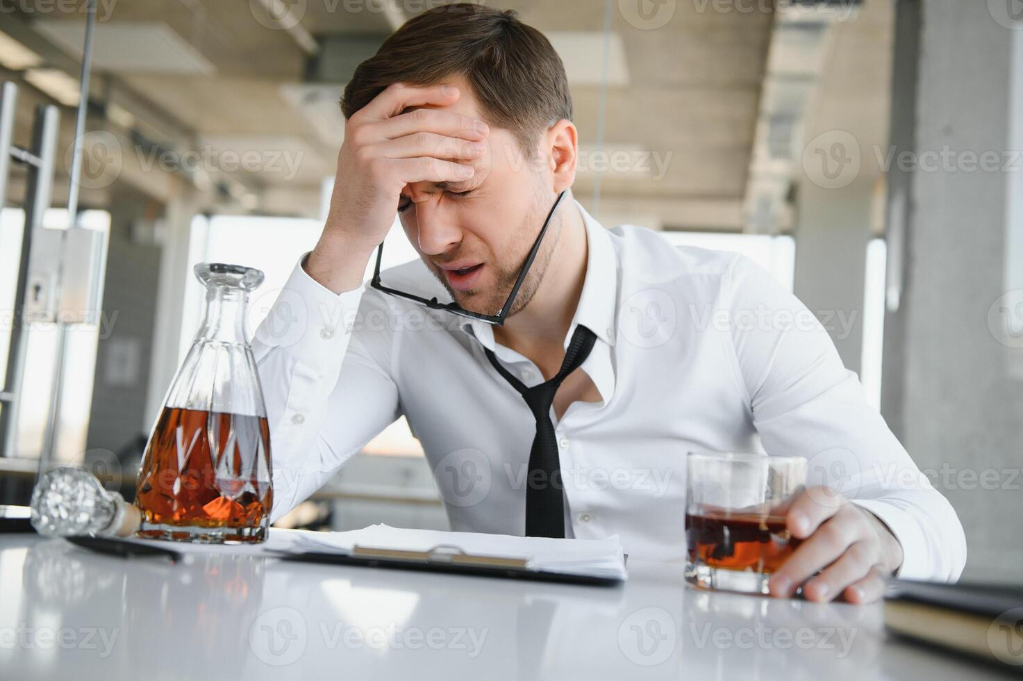 fatiga joven empresario sentado a lugar de trabajo y participación whisky botella, Bebiendo alcohol, bancarrota concepto. foto