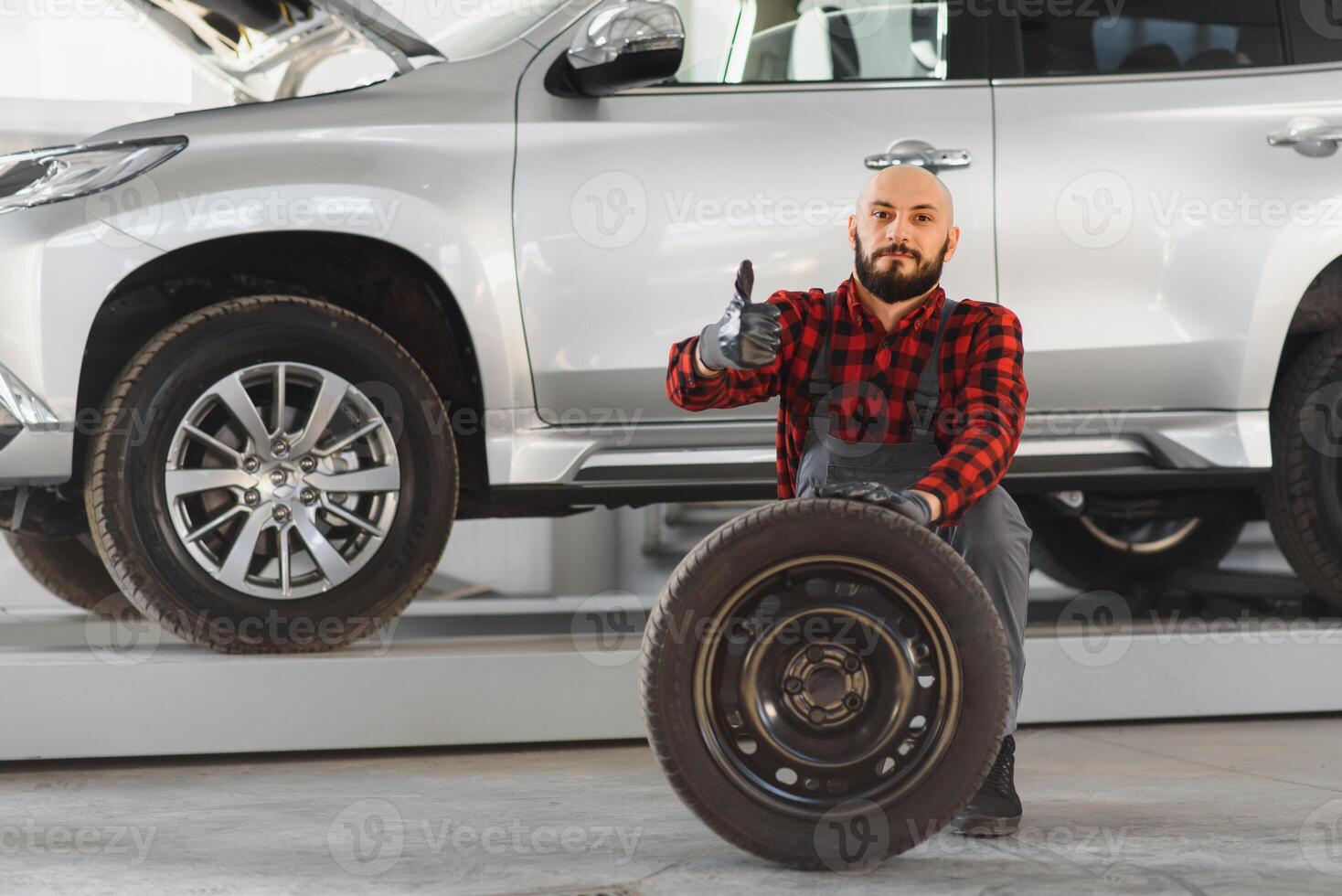 mecánico sosteniendo un neumático en el taller de reparación. sustitución de neumáticos de invierno y verano. foto