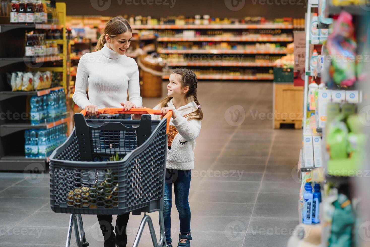 hermosa madre participación tienda de comestibles cesta con su niño caminando en supermercado. compras para saludable. foto