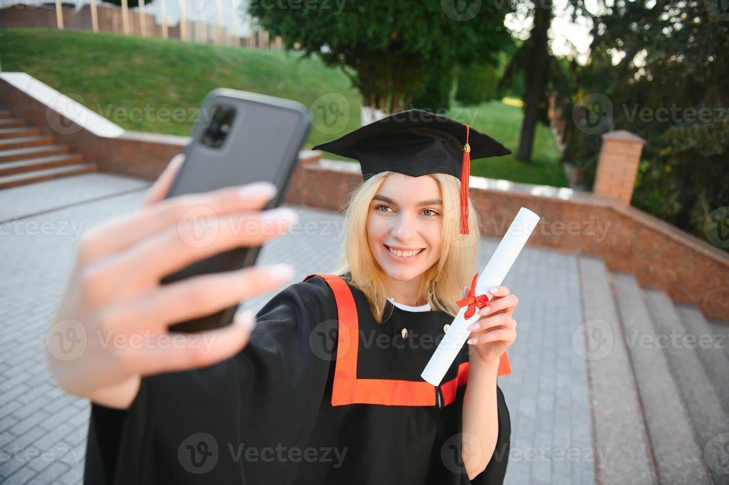 contento hembra estudiante participación Universidad diploma mientras tomando selfie después graduación ceremonia. foto