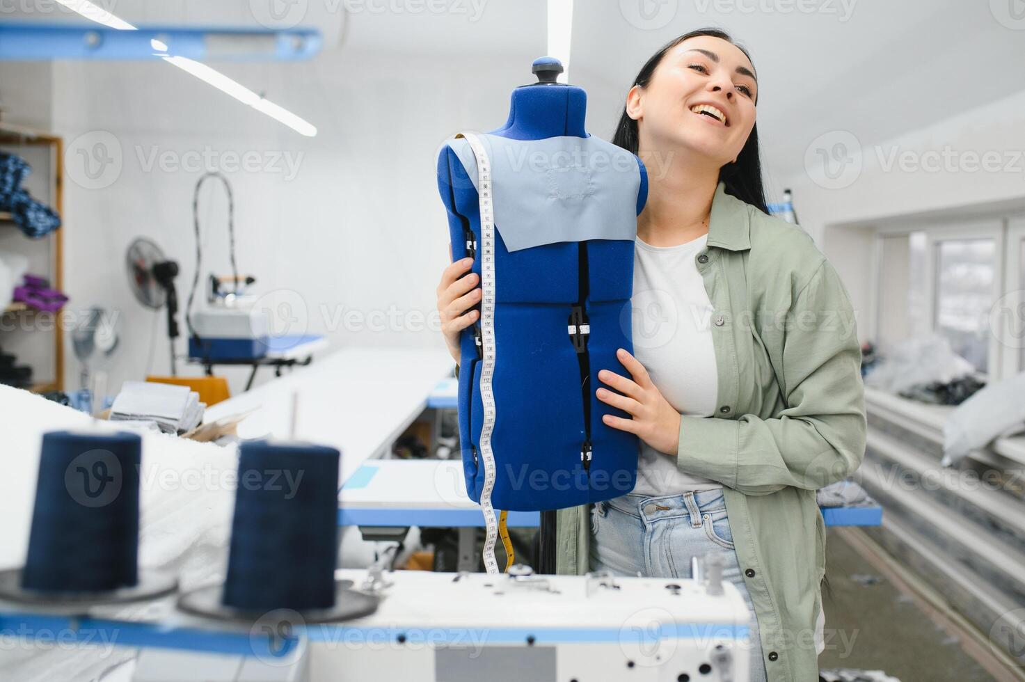 joven modista mujer cose ropa en trabajando mesa. sonriente costurera y su mano cerca arriba en taller. foto
