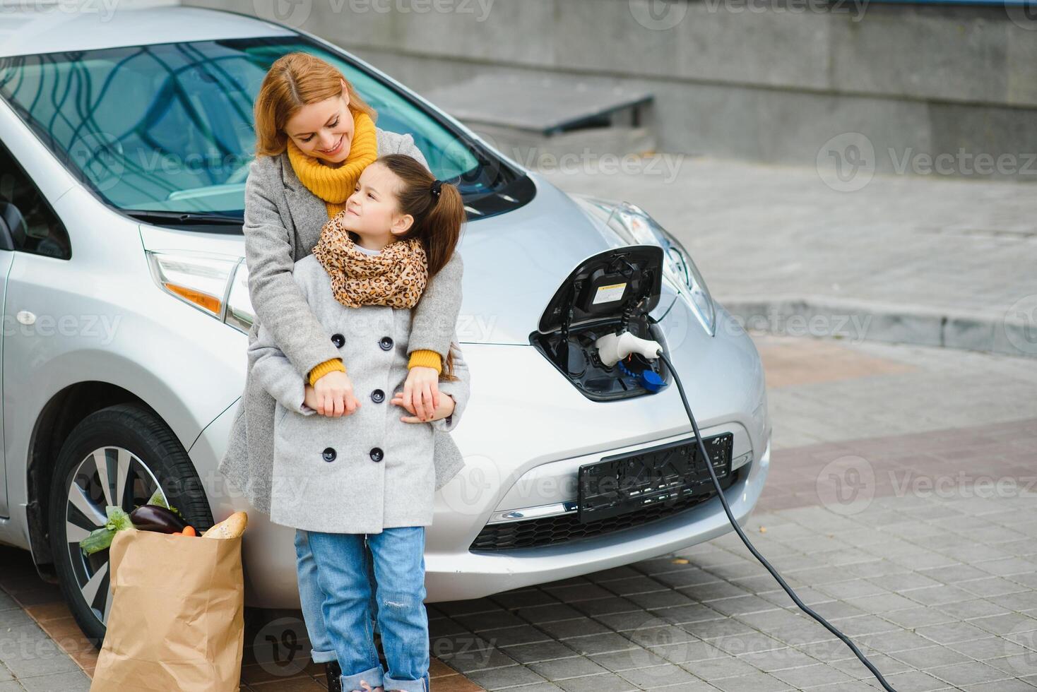 mother with daughter charging electro car at the electric gas station and speak on mobile phone photo