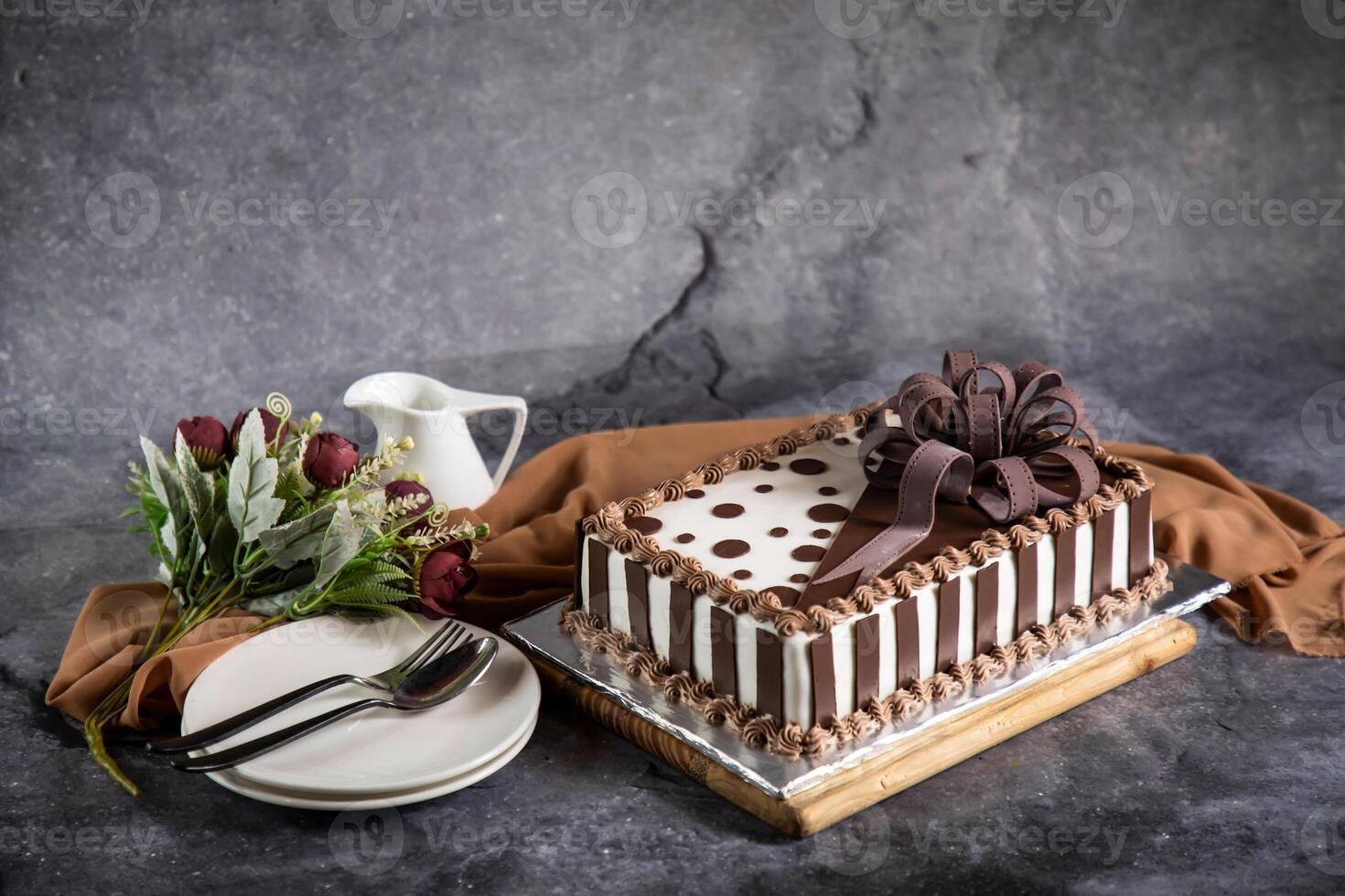 Square Chocolate Cake with rose flowers, spoon and fork served on board isolated on napkin side view of cafe baked food photo