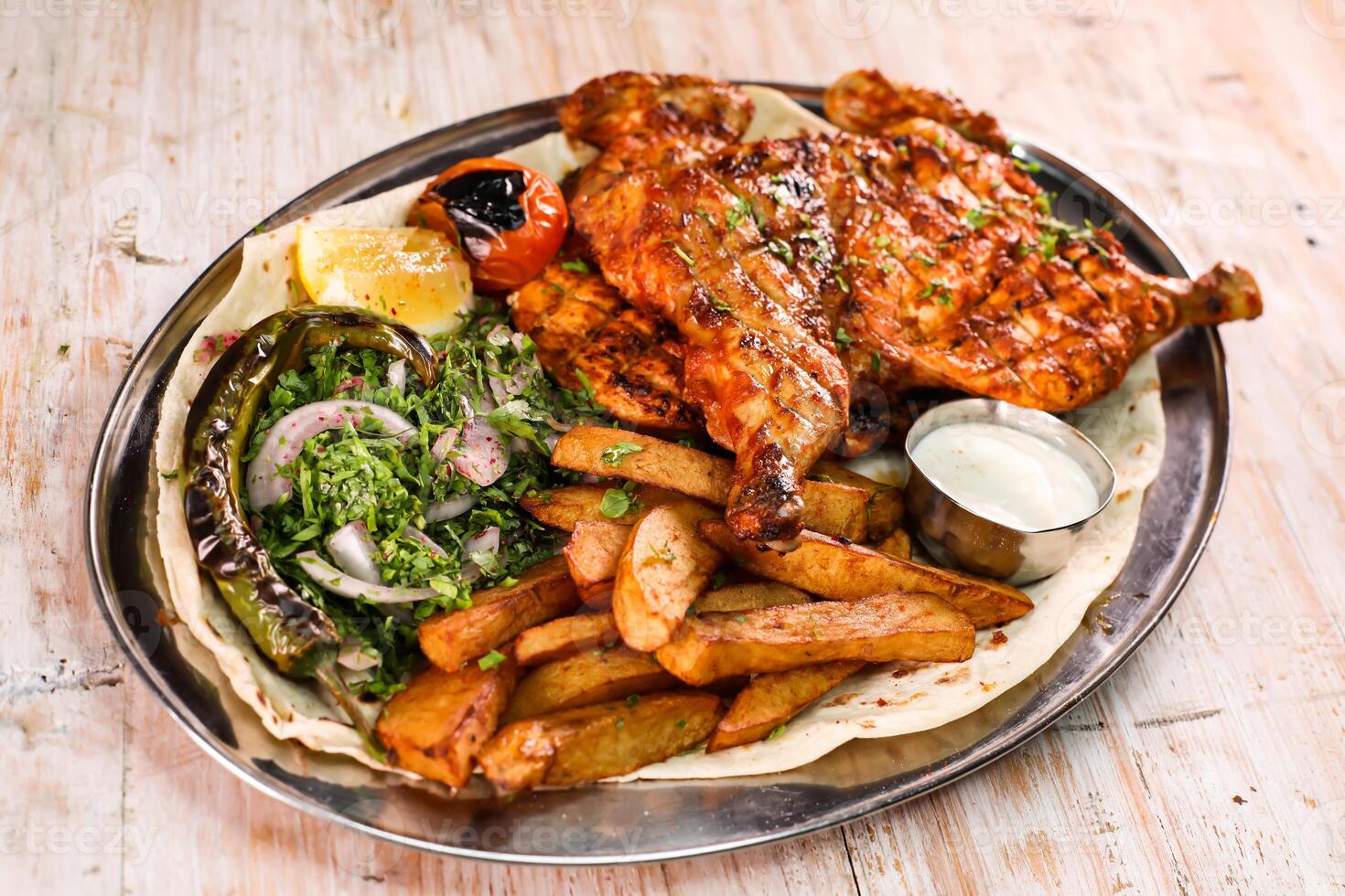 Full grilled chicken with salad, wedges, lemon and dip served in dish isolated on background top view of arabic food photo