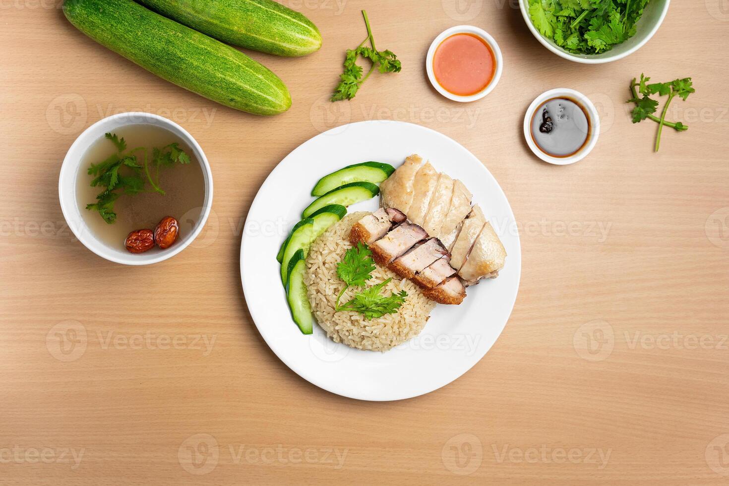 Steamed Chicken and Roast Pork Rice with raw cucumber, Coriander, salad, sauce and soup served in a dish isolated on wooden background top view photo