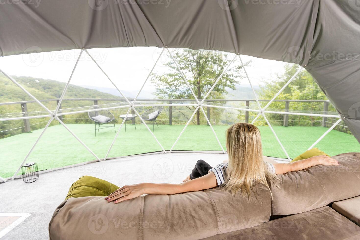 A woman sits in a geo dome glamping tent, looks at the nature. photo