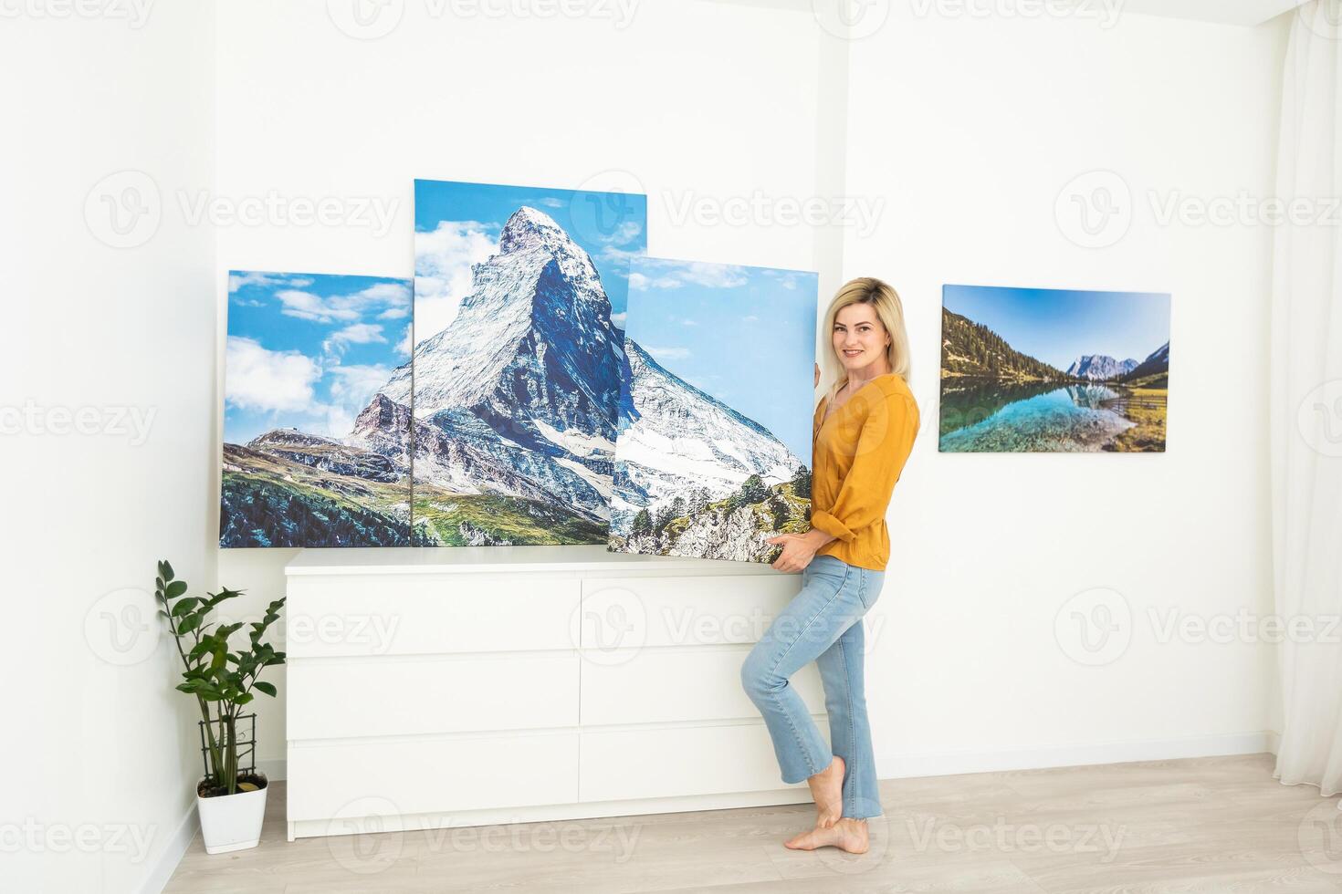 Canvas print with gallery wrap interior decor. Woman hangs landscape photography on white wall. Hands holding photo canvas print