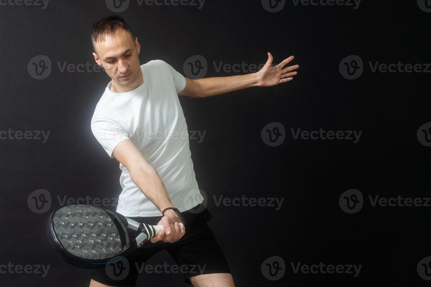 Portrait of man playing paddle tennis in position to hit a backhand ball black isolated background. Front view. photo