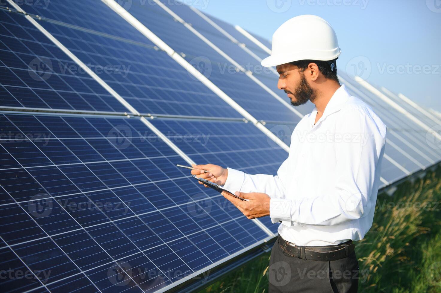 Portrait of Young indian male engineer standing near solar panels, with clear blue sky background, Renewable and clean energy. skill india, copy space. photo