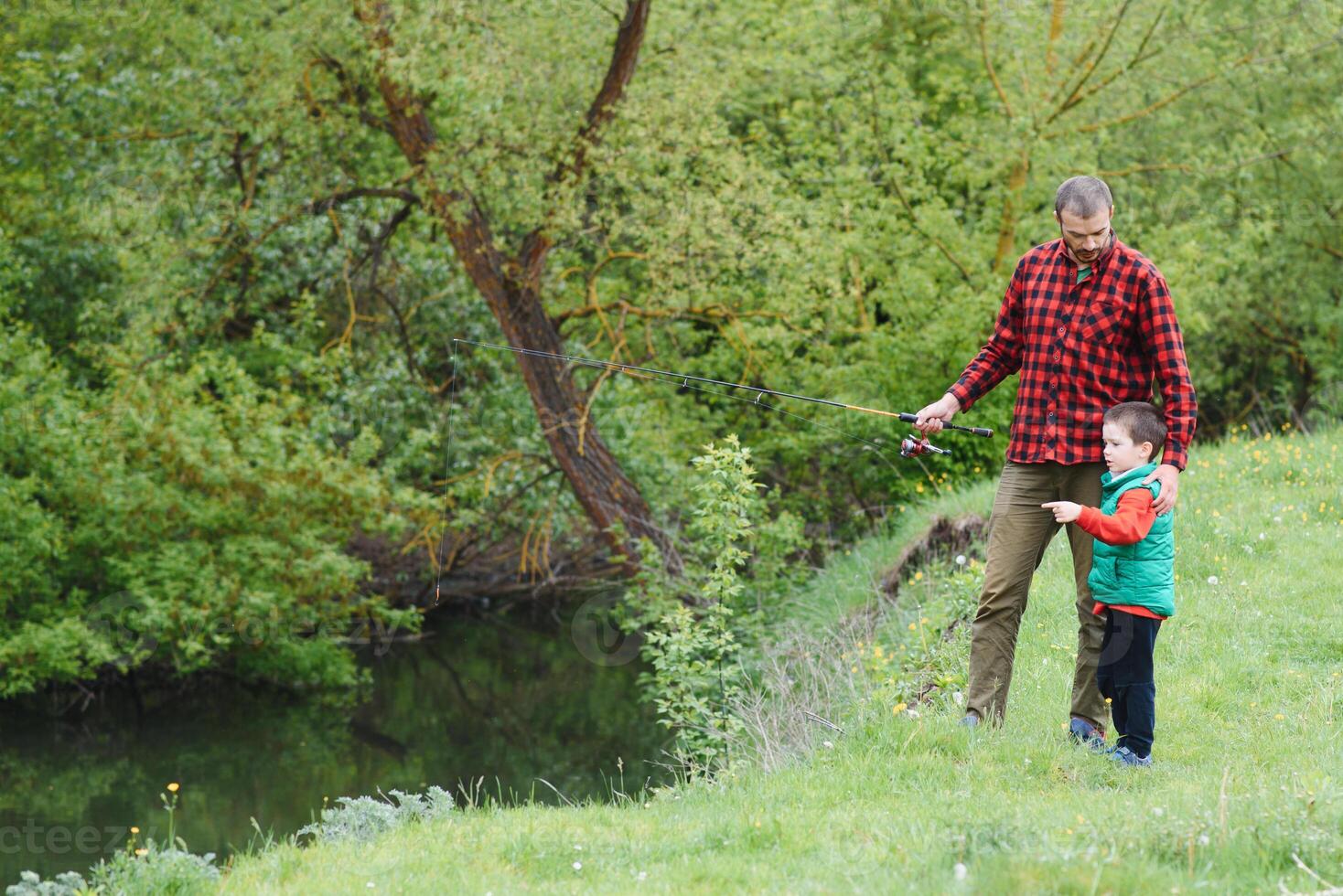 A father teaching his son how to fish on a river outside in summer sunshine photo