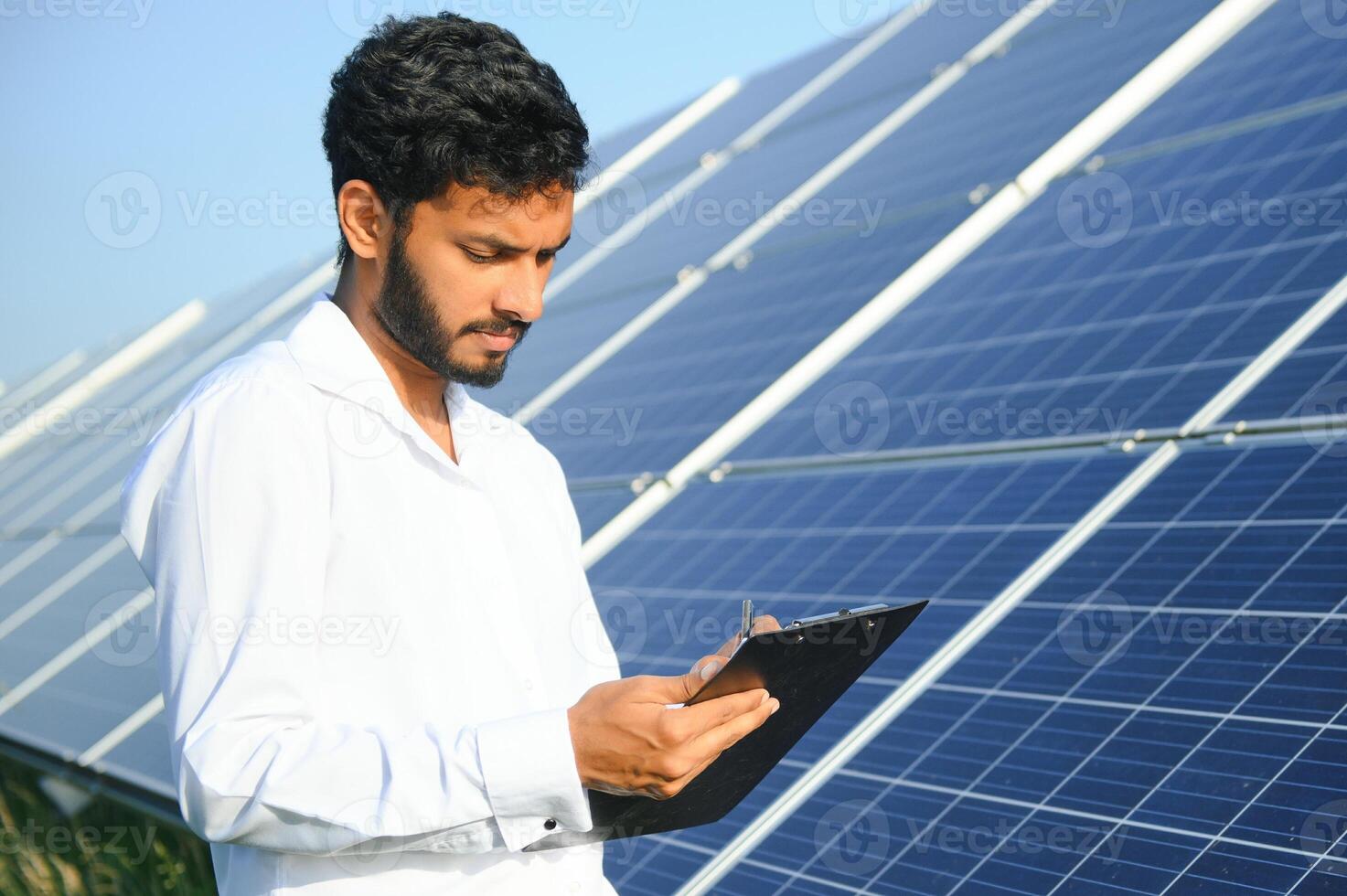 Portrait of Young indian male engineer standing near solar panels, with clear blue sky background, Renewable and clean energy. skill india, copy space. photo