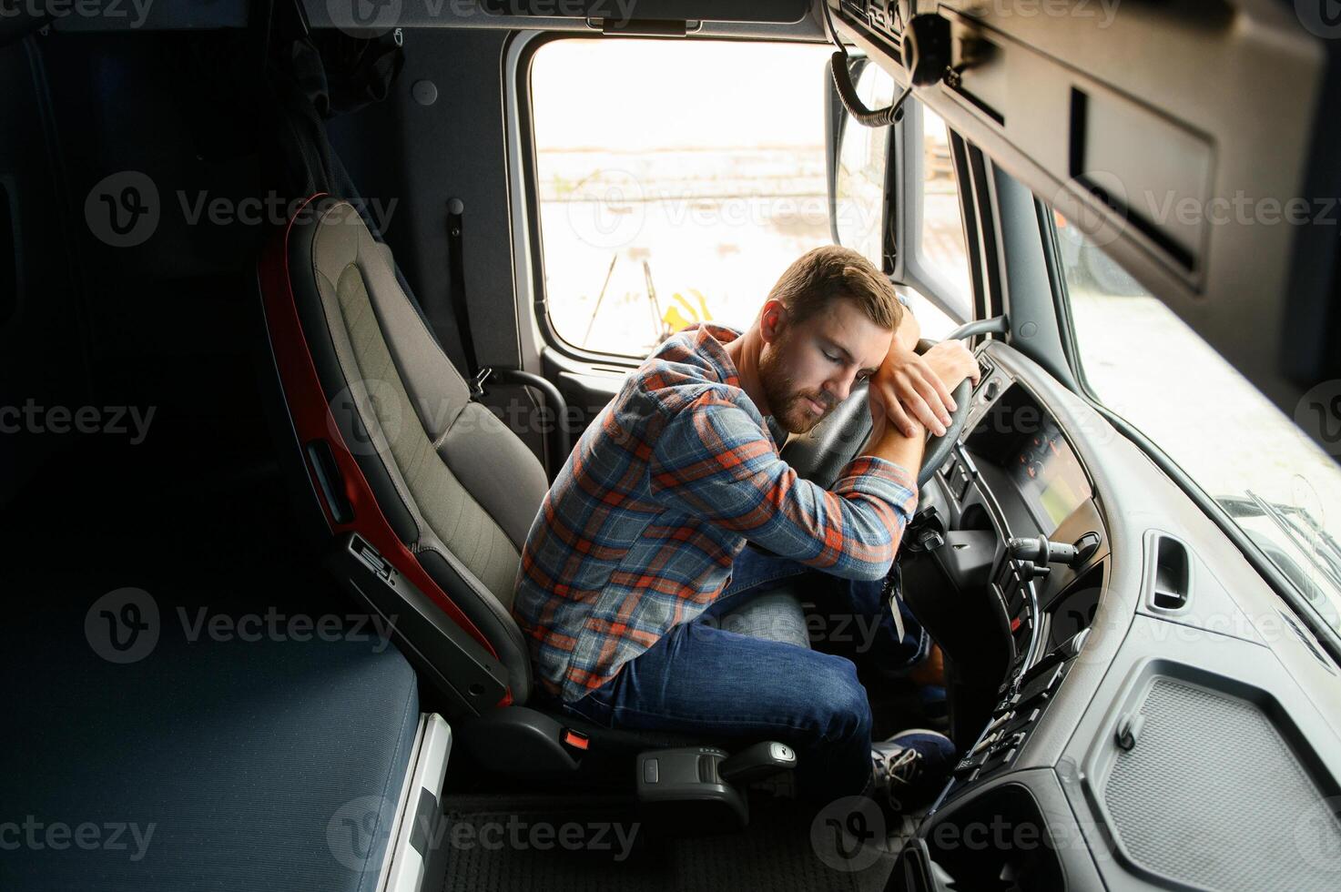 Tired of work. Sitting in the cabin. Young truck driver is with his vehicle at daytime. photo