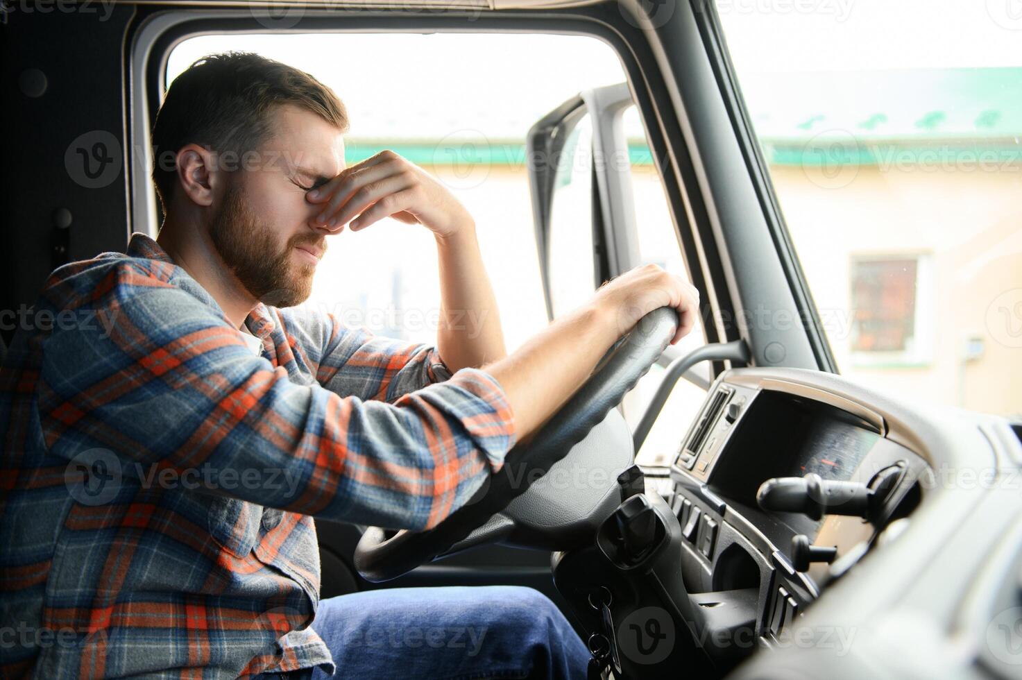 Tired of work. Sitting in the cabin. Young truck driver is with his vehicle at daytime. photo