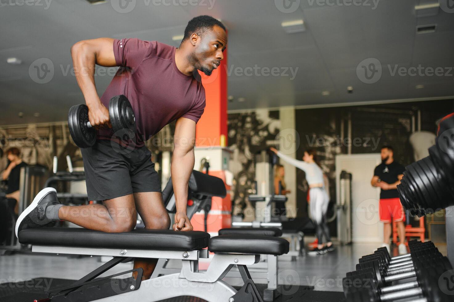 Hot african american young man bodybuilder lifting barbell at gym, working on his arms, looking at copy space. Black muscular shirtless guy having biceps workout session. Healthy lifestyle concept. photo