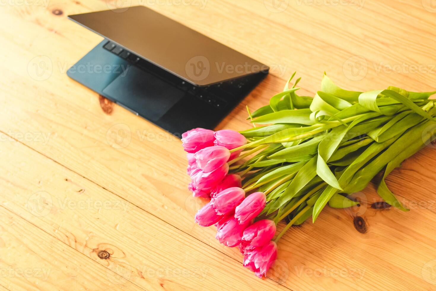 A bouquet of pink tulips flowers on a background of boards with an open laptop. photo