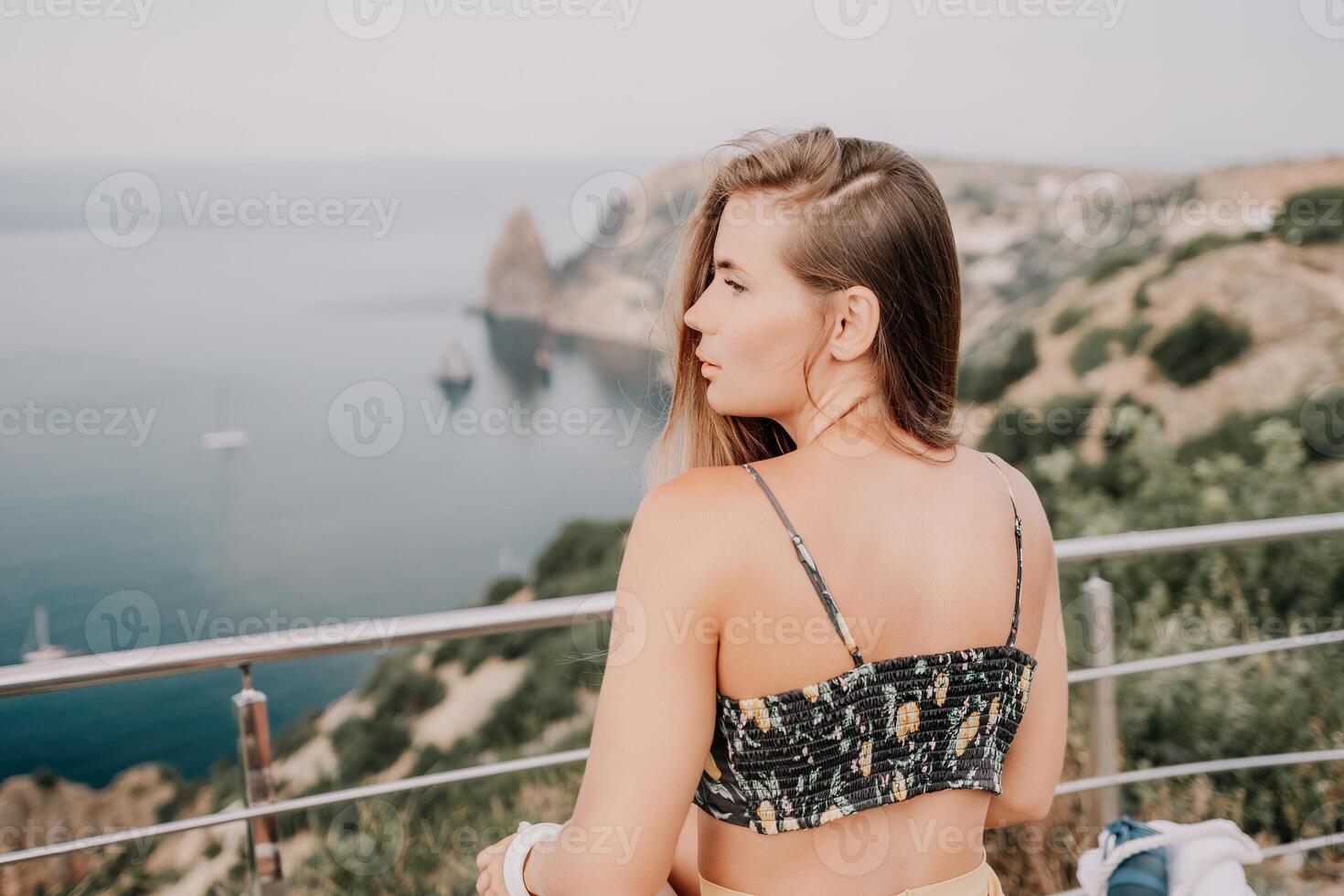 Woman travel sea. Happy tourist enjoy taking picture outdoors for memories. Woman traveler looks at the edge of the cliff on the sea bay of mountains, sharing travel adventure journey photo