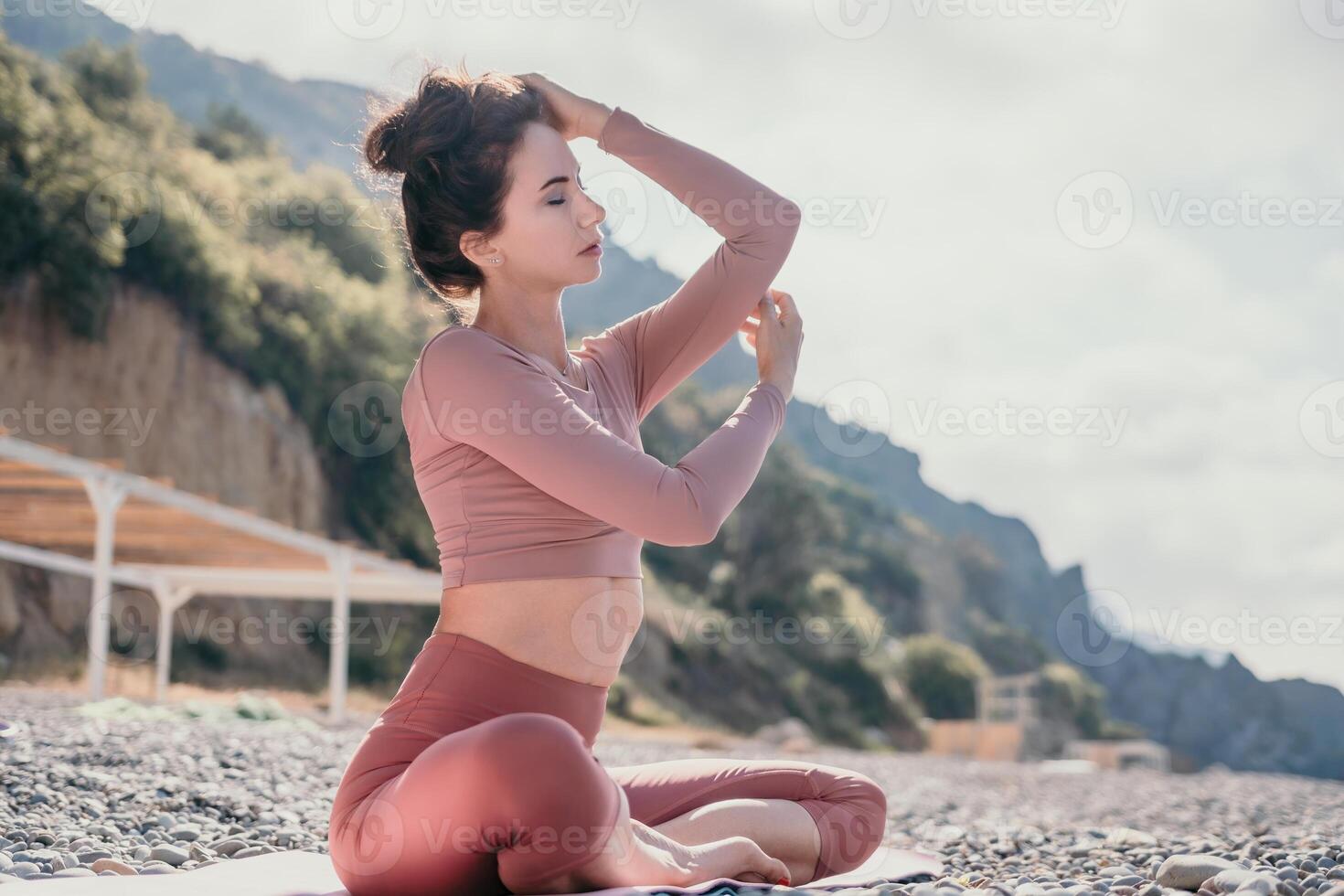 Middle aged well looking woman with black hair, fitness instructor in leggings and tops doing stretching and pilates on yoga mat near the sea. Female fitness yoga routine concept. Healthy lifestyle photo