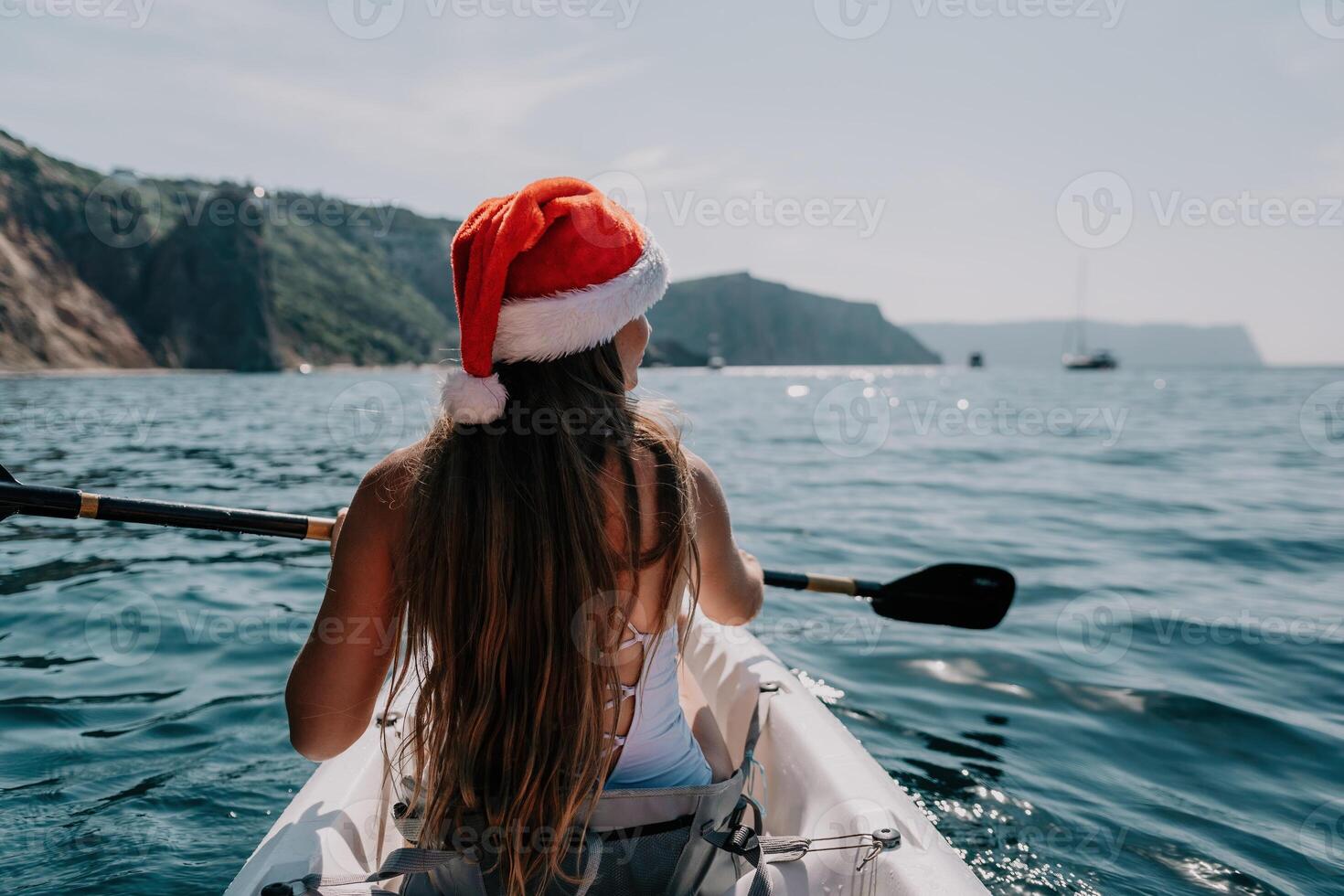 Woman in kayak back view. Happy young woman in Santa hat floating in kayak on calm sea. Summer holiday vacation and cheerful female people relaxing having fun on the boat. photo