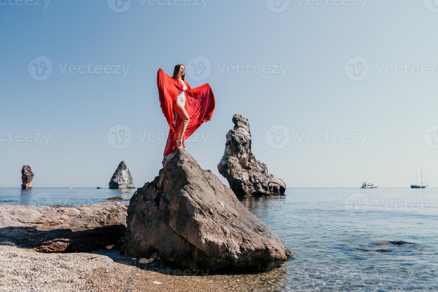 Woman travel sea. Young Happy woman in a long red dress posing on a beach near the sea on background of volcanic rocks, like in Iceland, sharing travel adventure journey photo