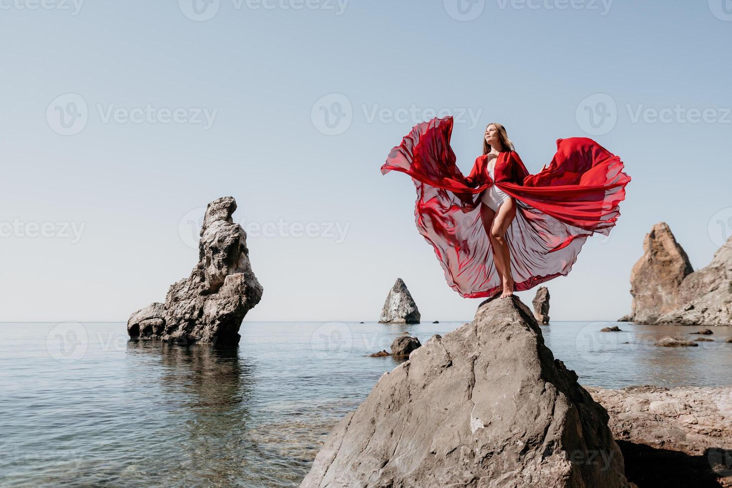 Woman travel sea. Young Happy woman in a long red dress posing on a beach near the sea on background of volcanic rocks, like in Iceland, sharing travel adventure journey photo
