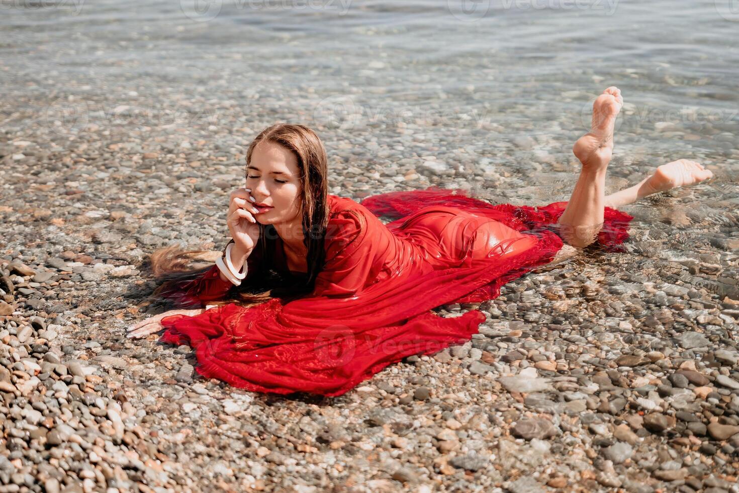 Woman travel sea. Happy tourist in red dress enjoy taking picture outdoors for memories. Woman traveler posing in sea beach, surrounded by volcanic mountains, sharing travel adventure journey photo