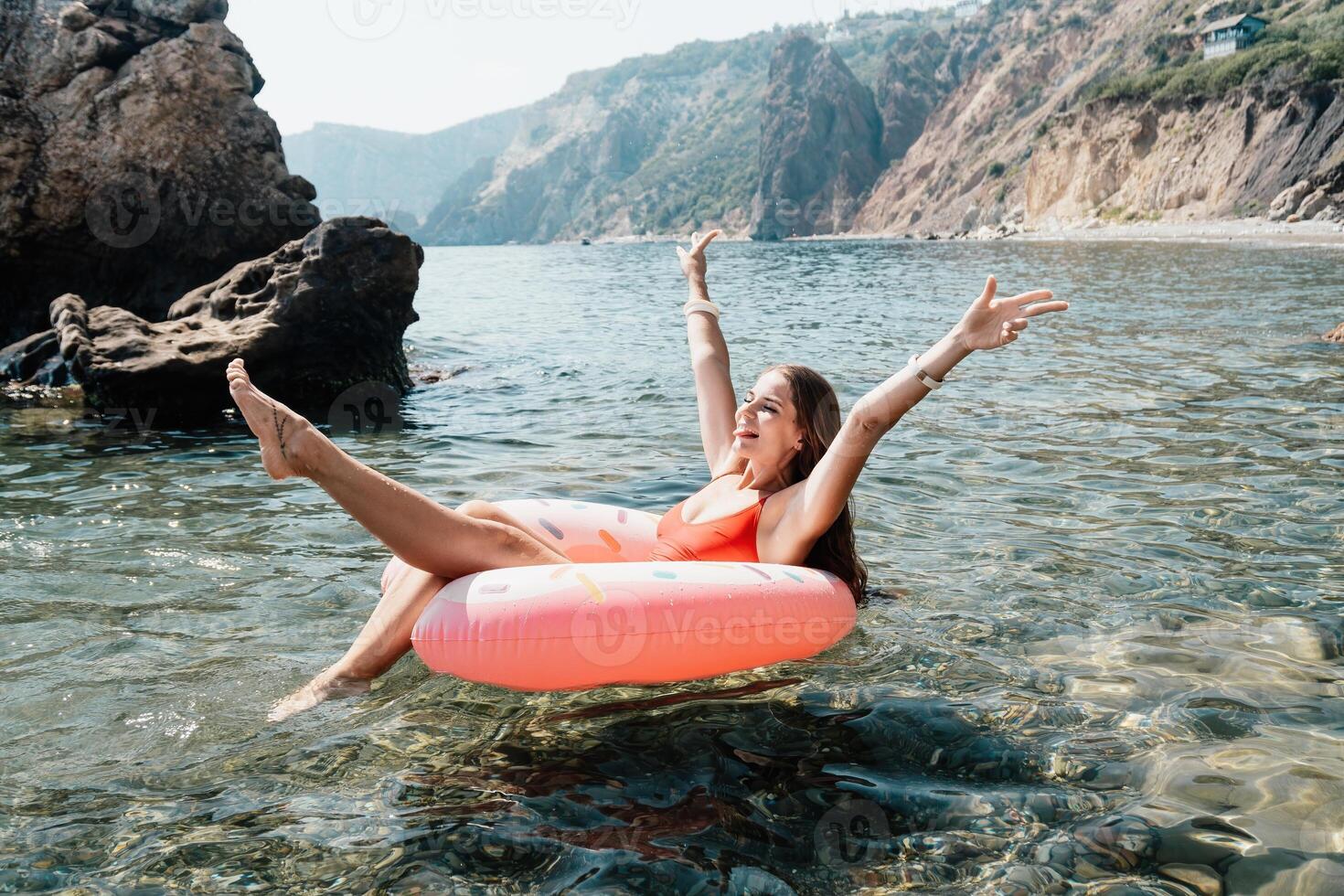 Woman summer sea. Happy woman swimming with inflatable donut on the beach in summer sunny day, surrounded by volcanic mountains. Summer vacation concept. photo
