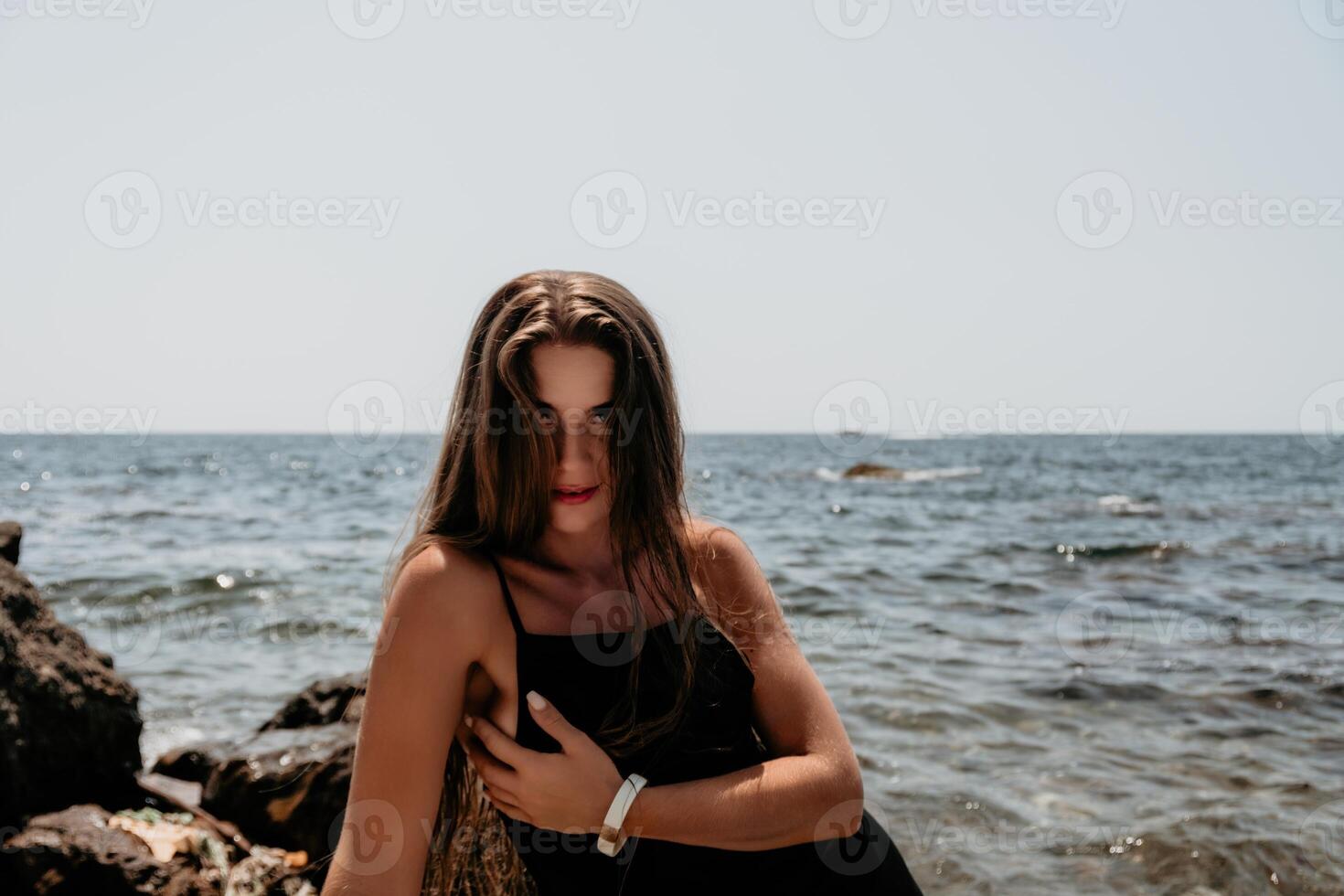 Woman summer travel sea. Happy tourist in hat enjoy taking picture outdoors for memories. Woman traveler posing on the beach at sea surrounded by volcanic mountains, sharing travel adventure journey photo