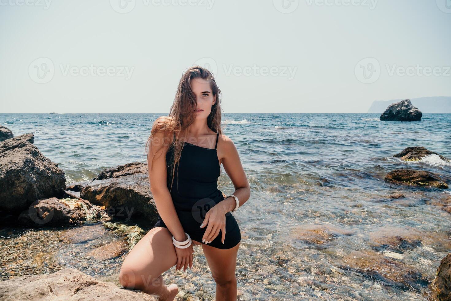 Woman summer travel sea. Happy tourist in hat enjoy taking picture outdoors for memories. Woman traveler posing on the beach at sea surrounded by volcanic mountains, sharing travel adventure journey photo