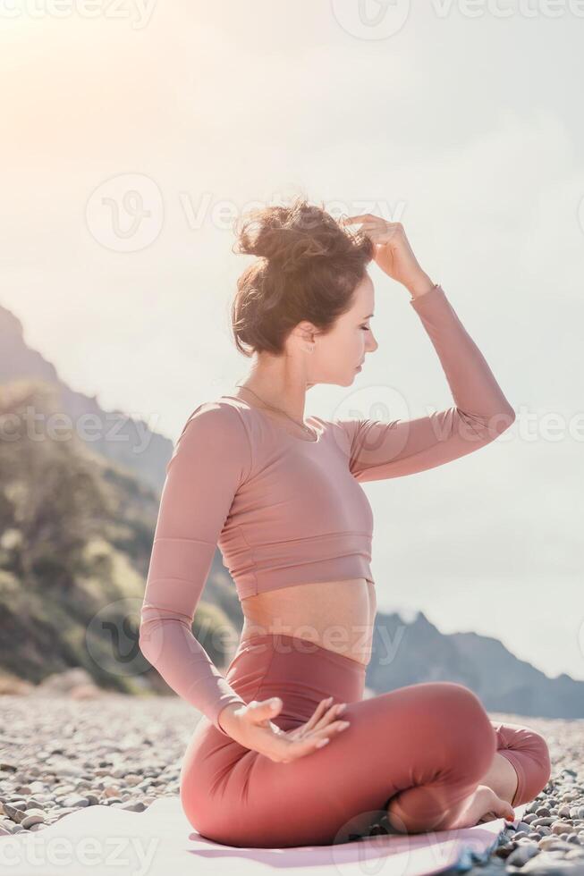 Middle aged well looking woman with black hair, fitness instructor in leggings and tops doing stretching and pilates on yoga mat near the sea. Female fitness yoga routine concept. Healthy lifestyle photo