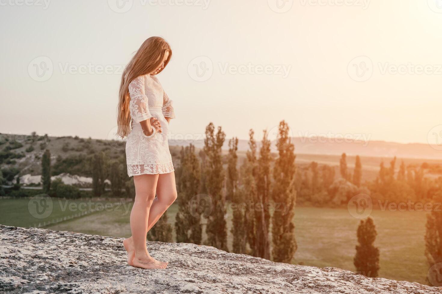 contento mujer en blanco boho vestir en puesta de sol en montañas. romántico mujer con largo pelo en pie con su espalda en el puesta de sol en naturaleza en verano con abierto manos. silueta. naturaleza. puesta de sol. foto