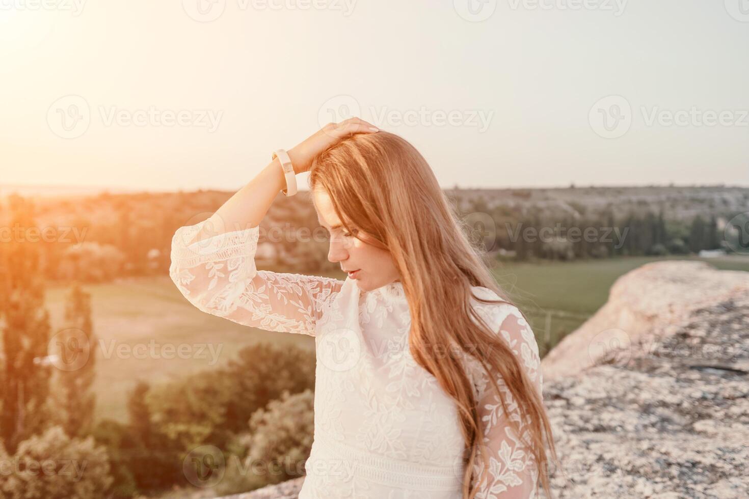 contento mujer en blanco boho vestir en puesta de sol en montañas. romántico mujer con largo pelo en pie con su espalda en el puesta de sol en naturaleza en verano con abierto manos. silueta. naturaleza. puesta de sol. foto