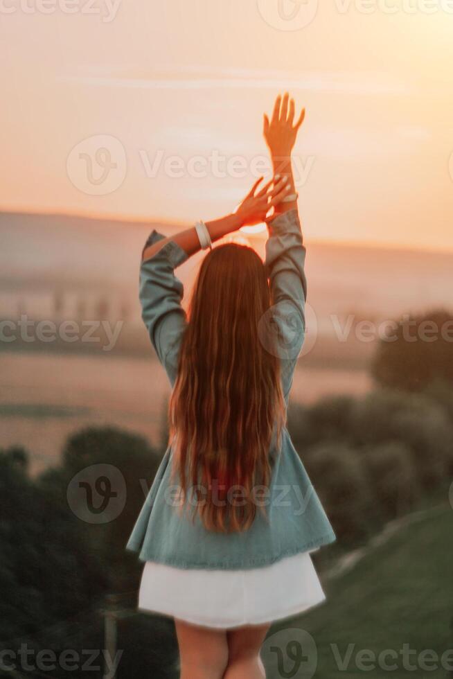 Happy woman standing with her back on the sunset in nature in summer with open hands. Romantic beautiful bride in white boho dress posing with mountains on sunset photo