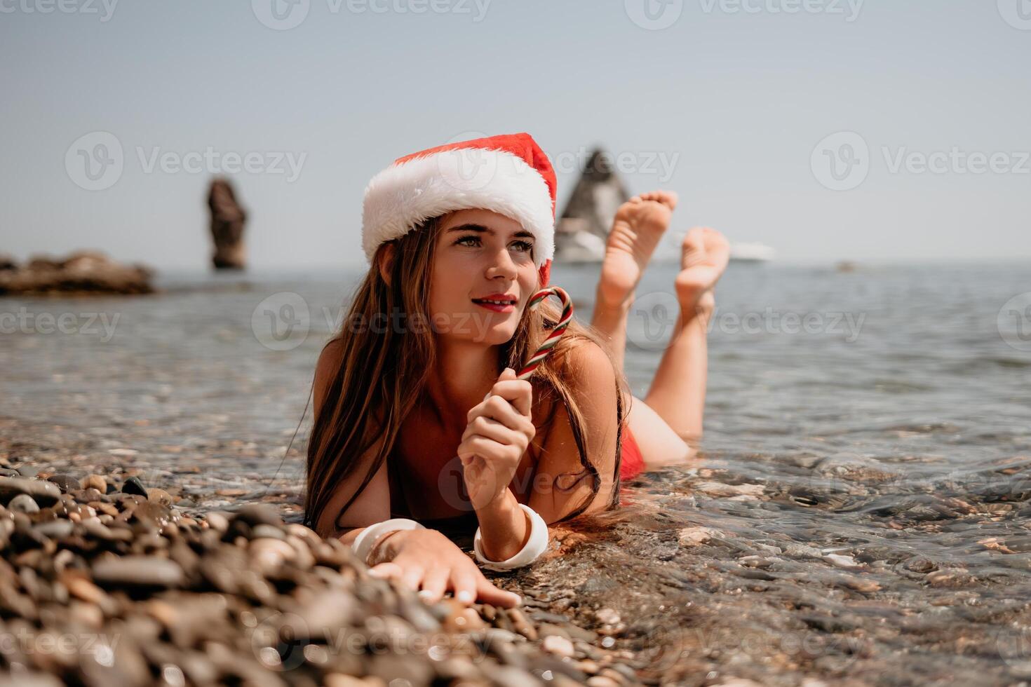Woman travel sea. Happy tourist enjoy taking picture on the beach for memories. Woman traveler in Santa hat looks at camera on the sea bay, sharing travel adventure journey photo