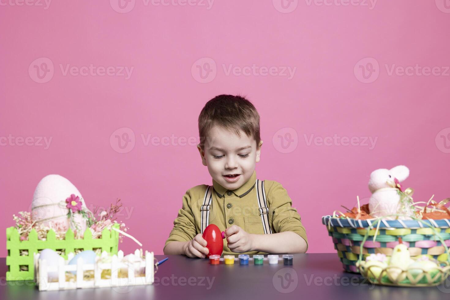 Adorable little youngster making lovely arrangements for Easter Sunday and painting eggs with stamps and brushes. Delightful child likes using crafting materials to decorate in studio. photo