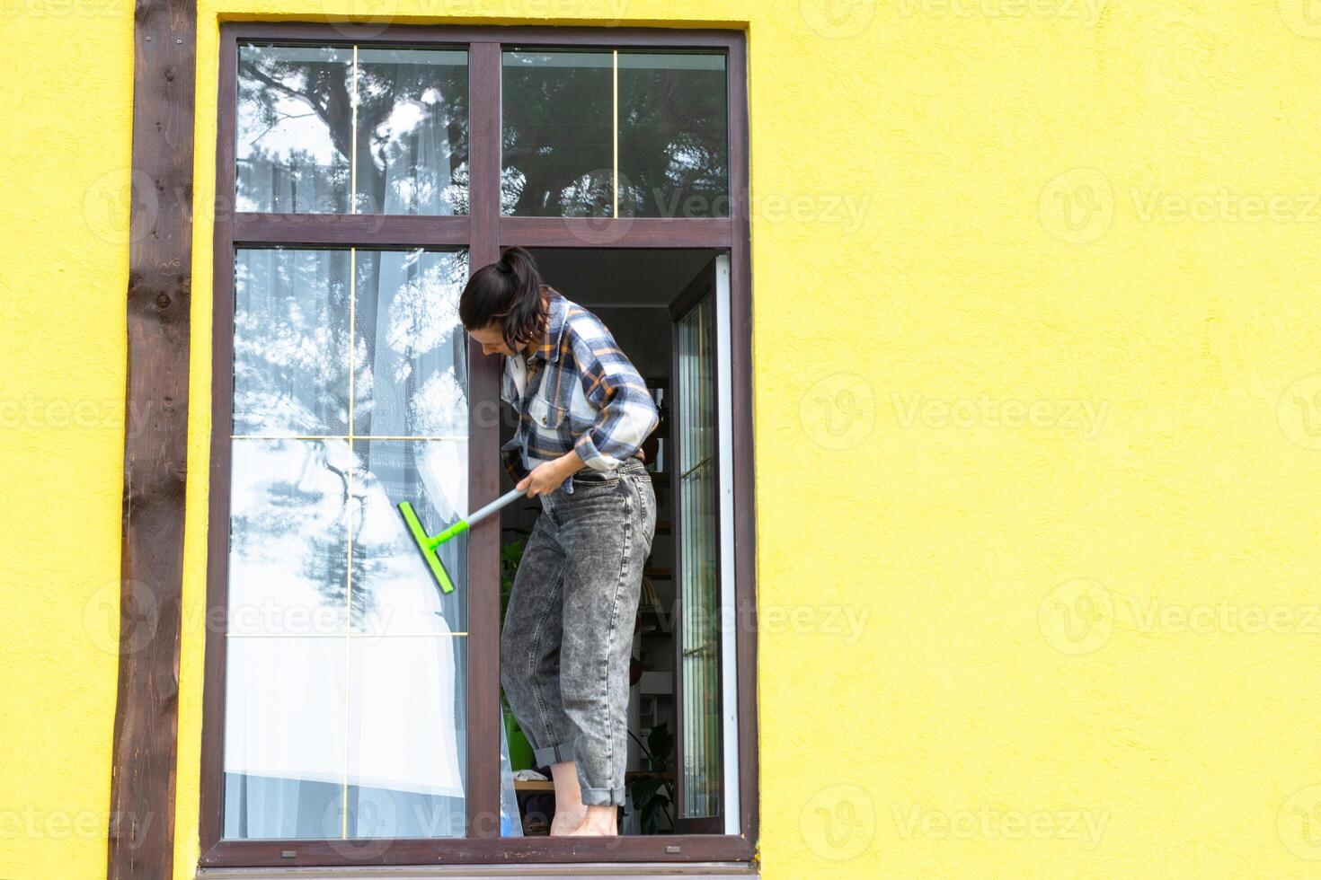 A woman manually washes the window of the house with a rag with a spray cleaner and a mop outside. Safety at height, restoring order and cleanliness in the spring, cleaning service photo
