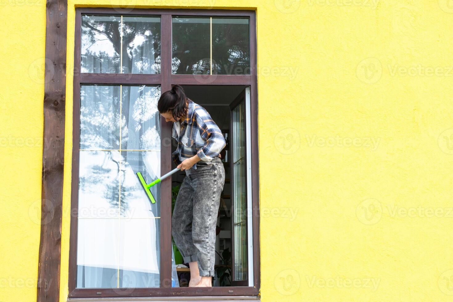 un mujer a mano lavados el ventana de el casa con un trapo con un rociar limpiador y un fregona afuera. la seguridad a altura, restaurar orden y limpieza en el primavera, limpieza Servicio foto