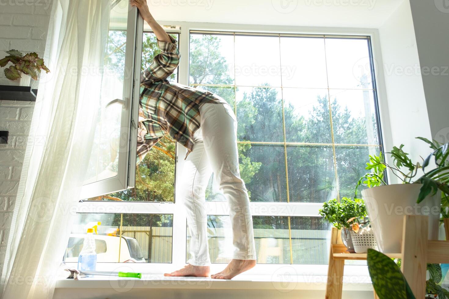 Woman manually washes the window of the house with a rag with spray cleaner and mop inside the interior with white curtains. Restoring order and cleanliness in the spring, cleaning servise photo