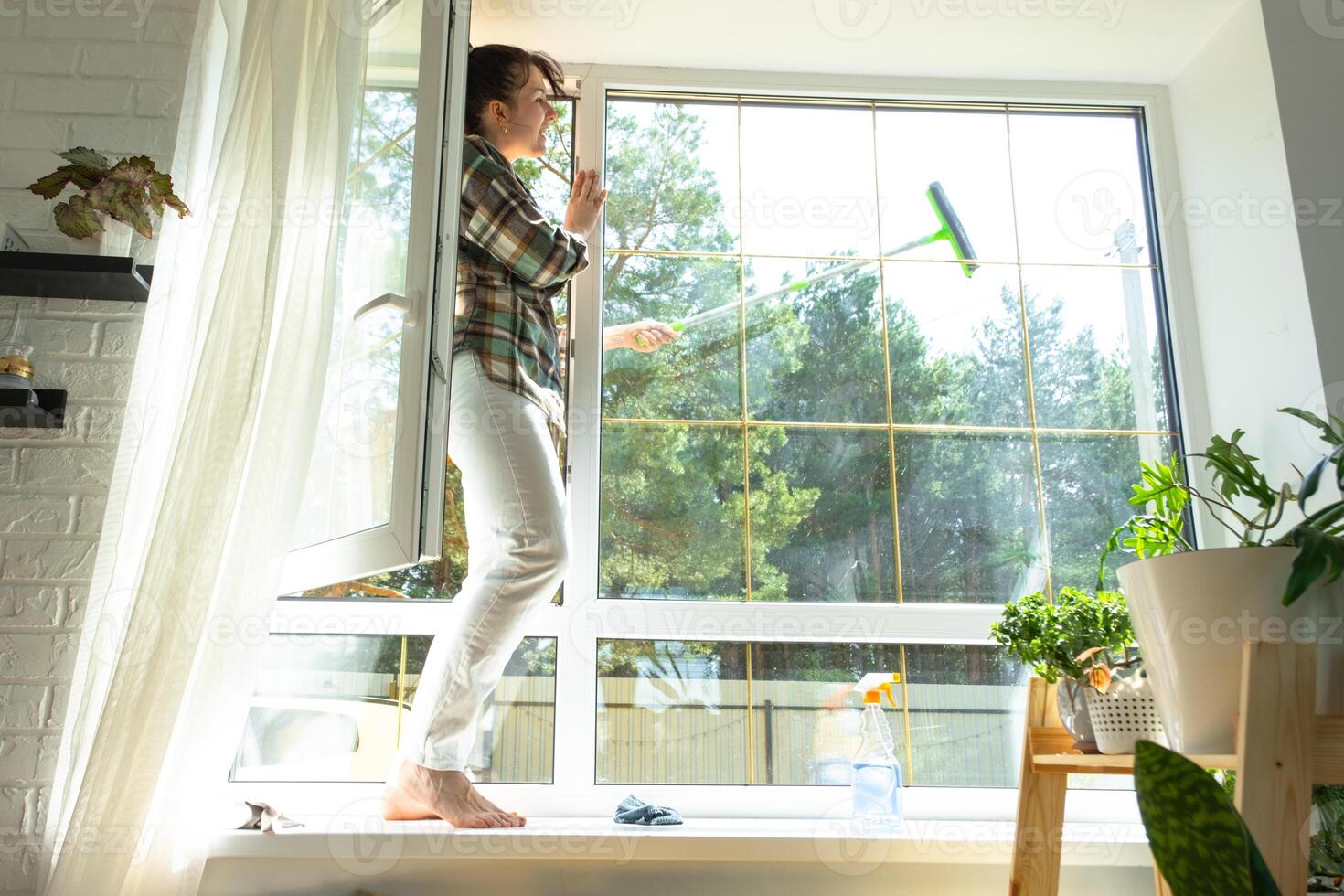 Woman manually washes the window of the house with a rag with spray cleaner and mop inside the interior with white curtains. Restoring order and cleanliness in the spring, cleaning servise photo