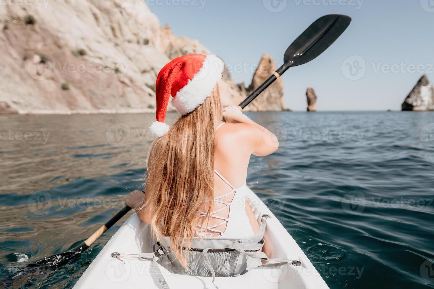 Woman in kayak back view. Happy young woman in Santa hat floating in kayak on calm sea. Summer holiday vacation and cheerful female people relaxing having fun on the boat. photo