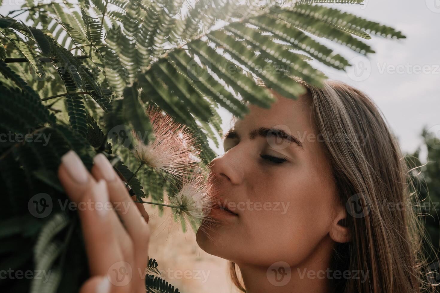 Beauty portrait of happy woman closeup. Young girl smelling Chinese acacia pink blossoming flowers. Portrait of young woman in blooming spring, summer garden. Romantic vibe. Female and nature photo